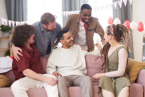 Free A mixed group of friends smiling and conversing on a sofa, showcasing joy and diversity. Stock Photo