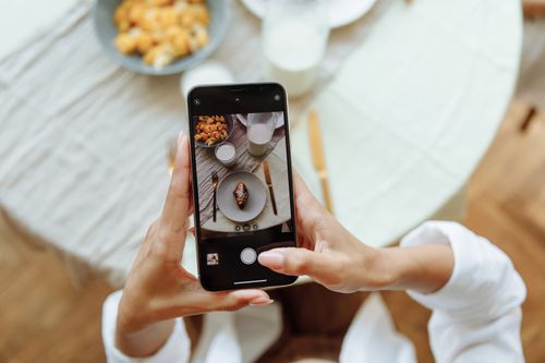 Free A person taking a photo of a breakfast setup with a smartphone on a table indoors. Stock Photo