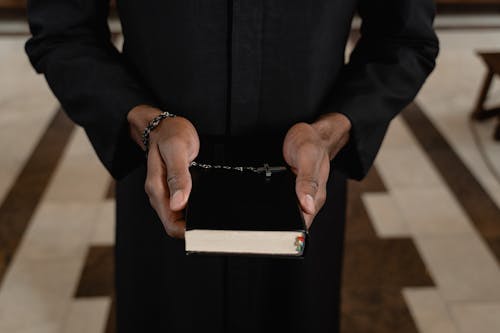 Free A Close-Up Shot of a Priest Holding a Bible and a Rosary Stock Photo