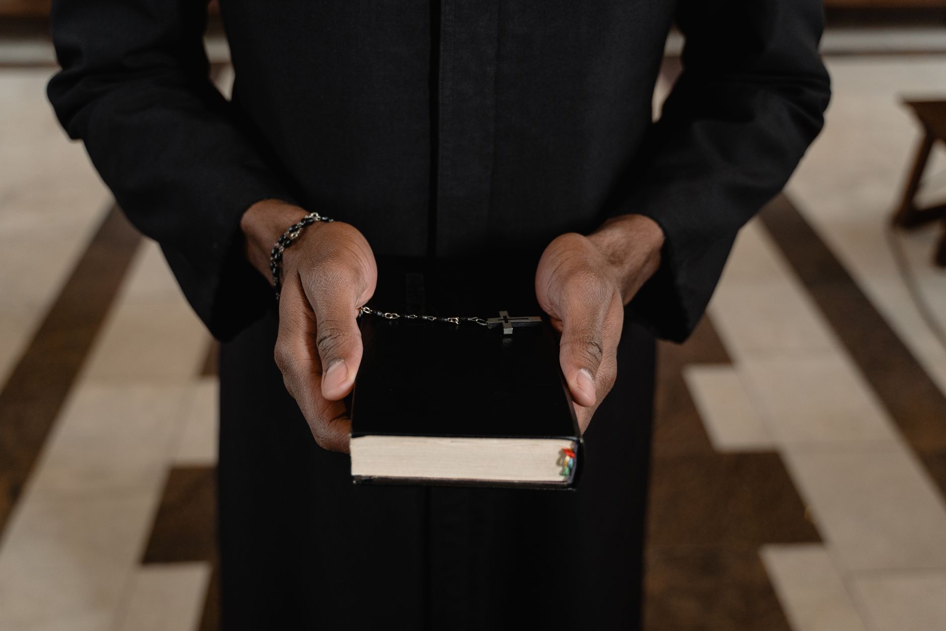 A priest's hands holding a Bible and rosary beads, symbolizing faith.
