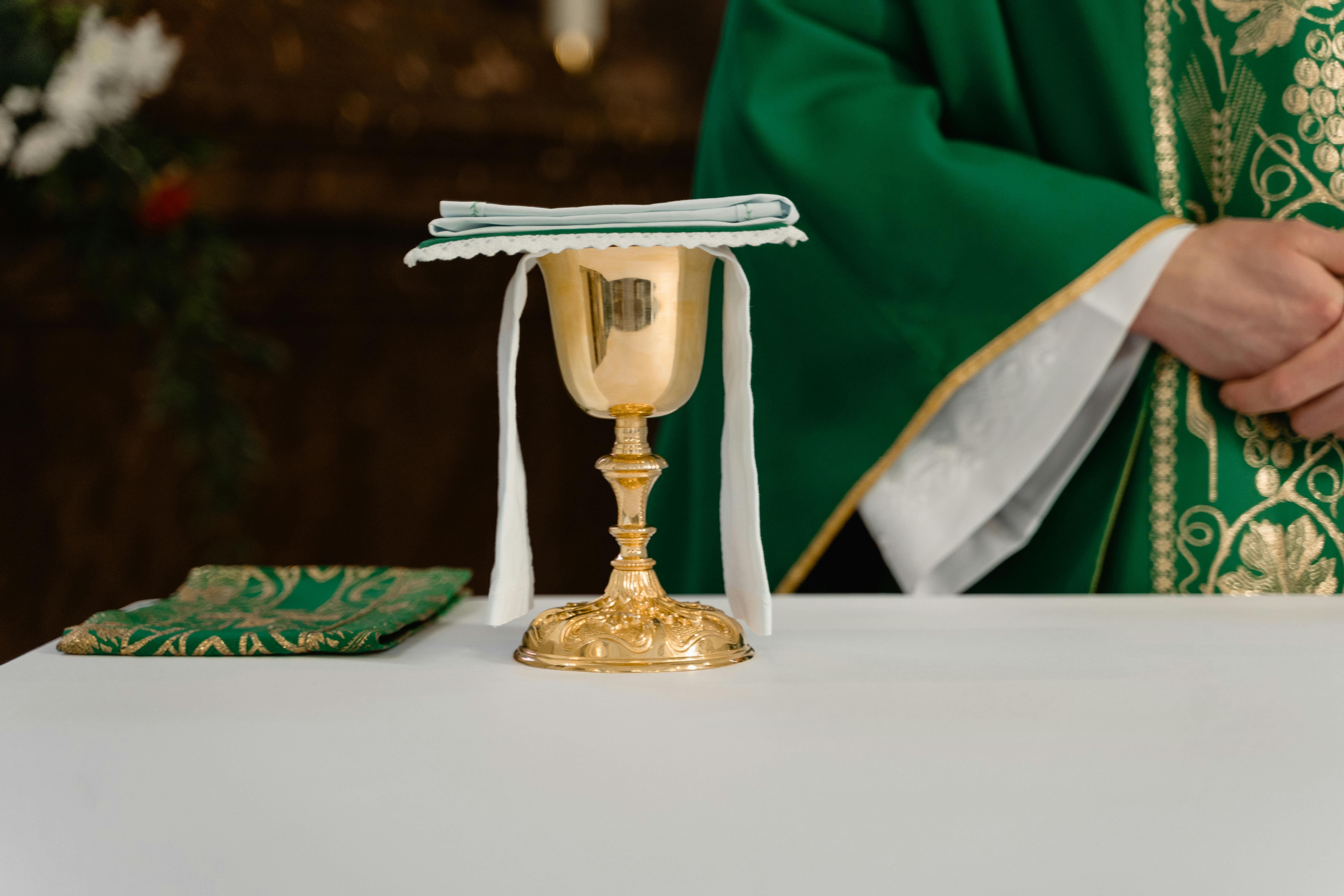 golden chalice on table beside a priest in green chasuble