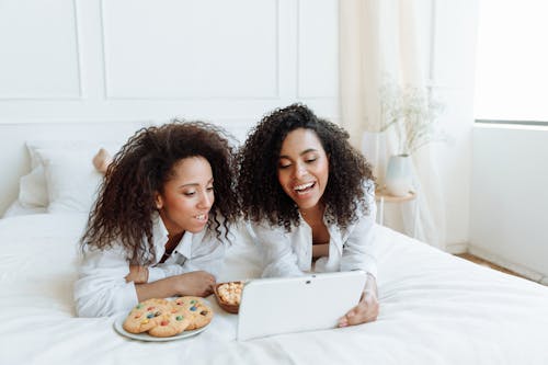 Two Women with Curly Hairs Watching on a Digital Tablet with Snacks