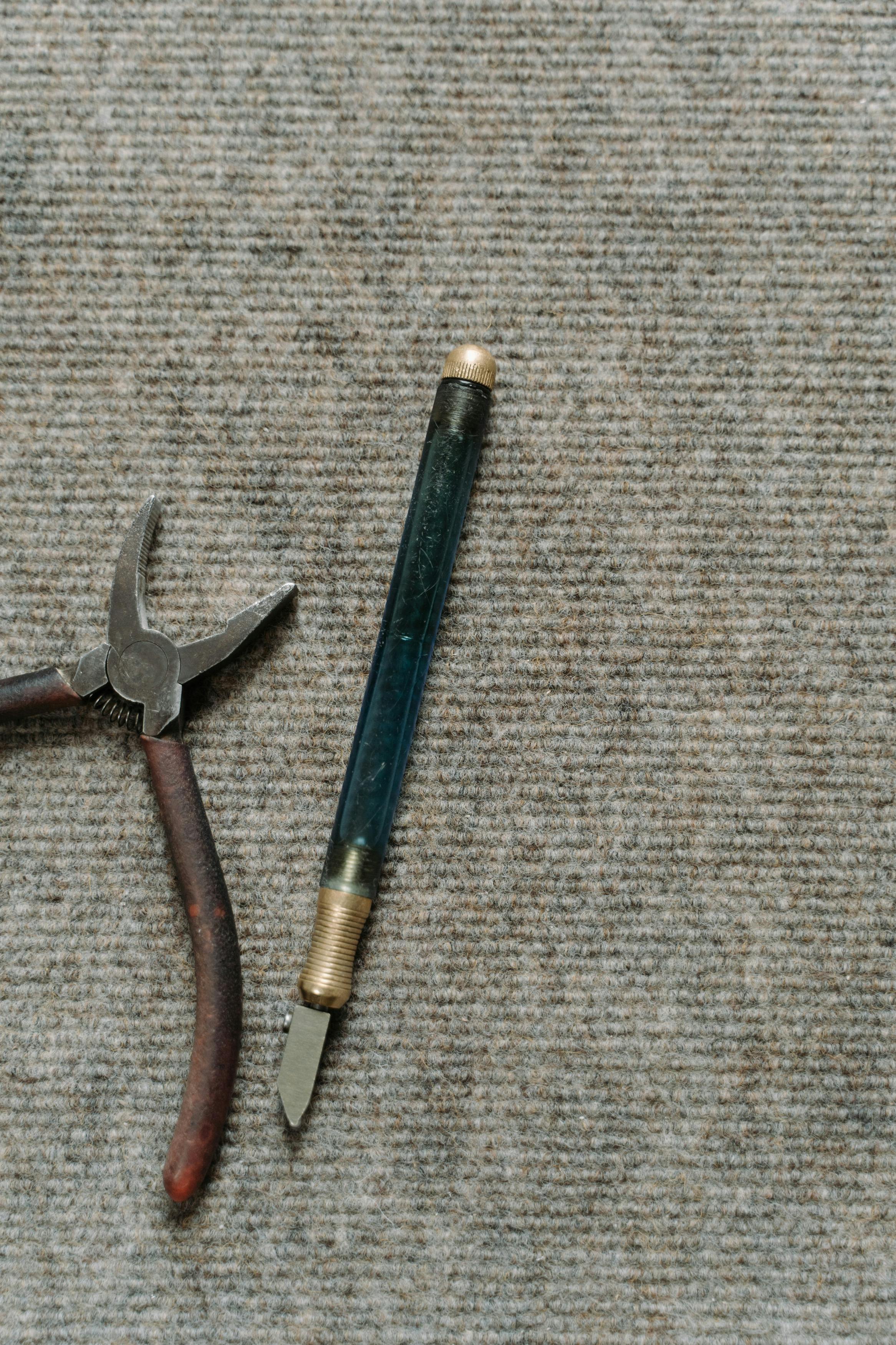 Close-up image of a glass cutter and pliers on a textured carpet surface.