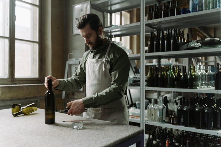 A Bearded Man Heating A Wine Bottle With A Blow Torch