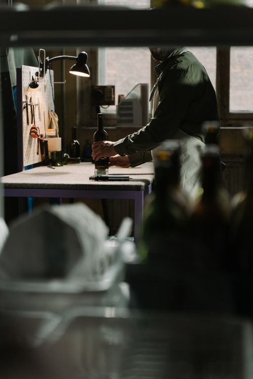 Free A craftsman reshapes glass bottles in a dimly lit workshop setting, showcasing handcrafting skills. Stock Photo