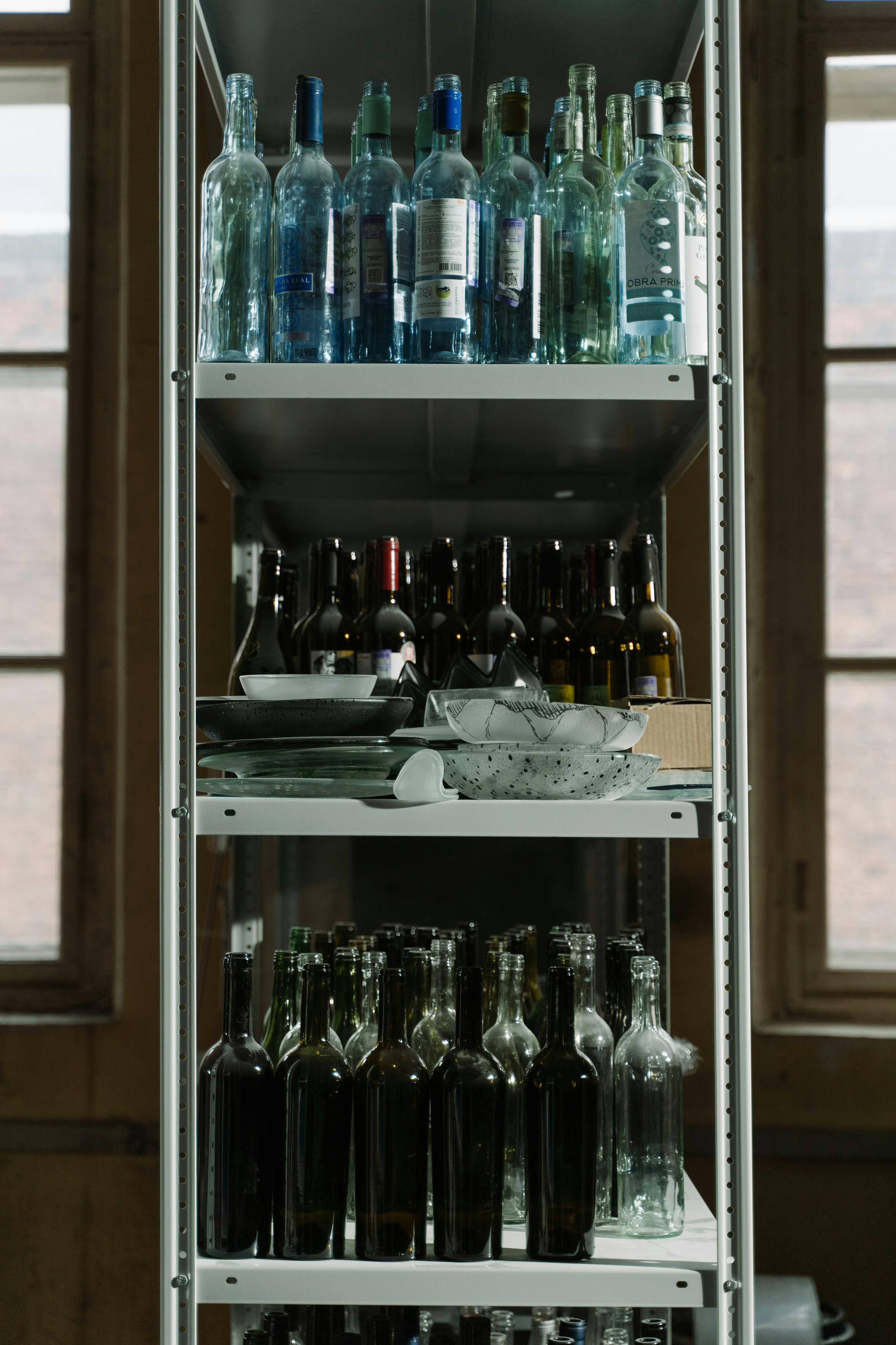 A variety of glass bottles neatly arranged on a multi-level shelf indoors.