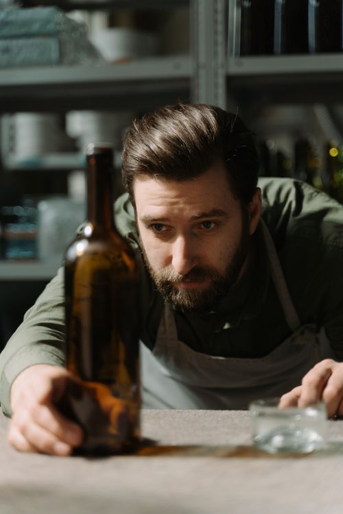 Free A focused man carefully examines a glass bottle in a workshop environment. Stock Photo