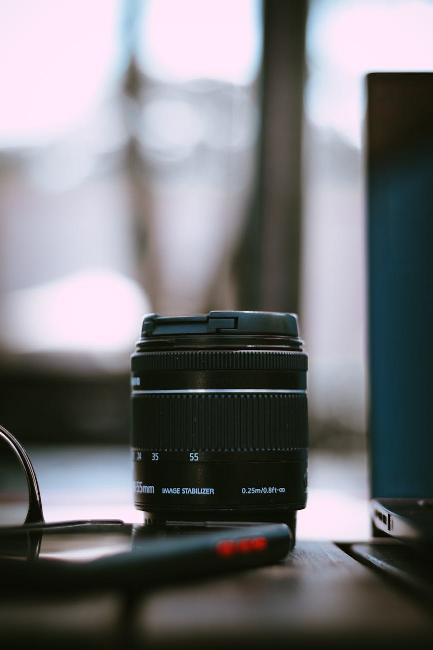 Detailed shot of a camera lens placed beside a laptop, highlighting photography equipment.