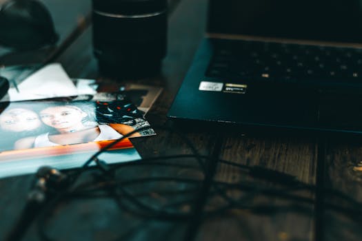 Artistic close-up of printed photos and a laptop on a rustic wooden surface.