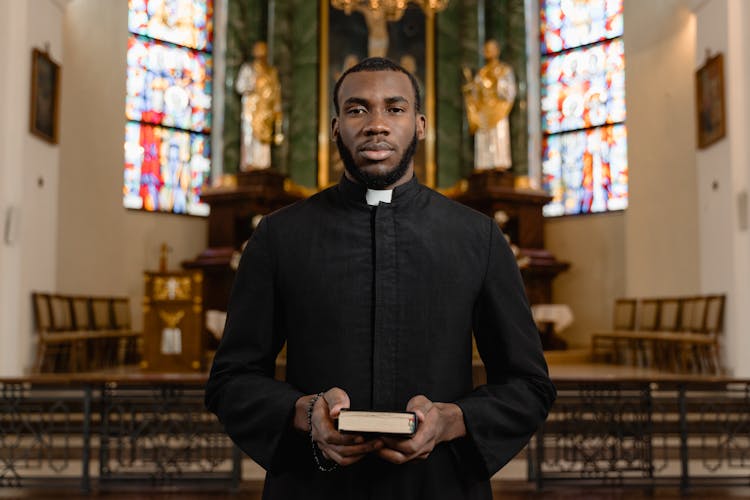 A Man In A Cassock Holding A Bible