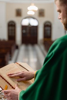 A priest in green robe reading the Holy Bible in a church setting, focusing on scripture.