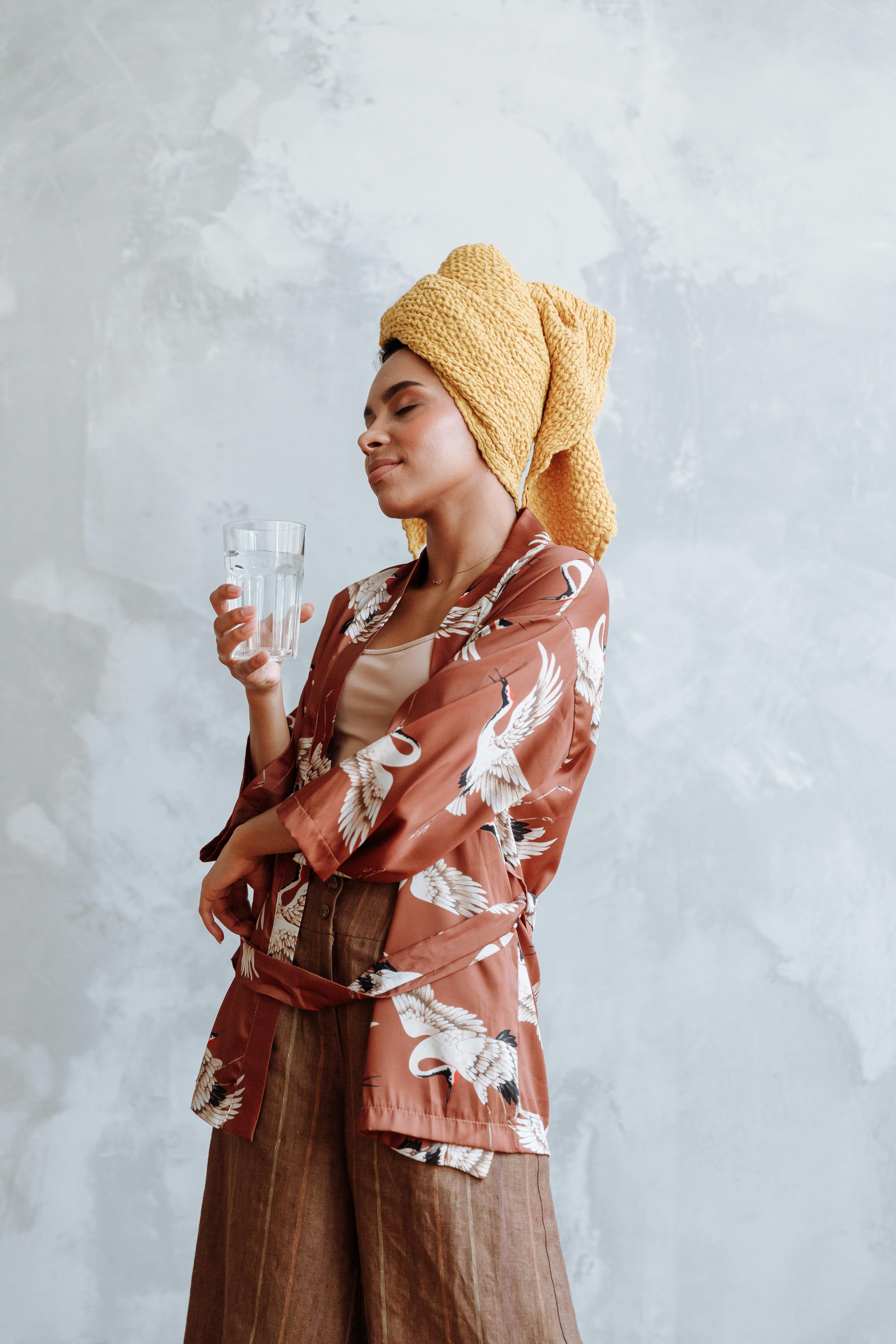 Woman with a towel on her head holding a glass of water, showcasing relaxation and style indoors.