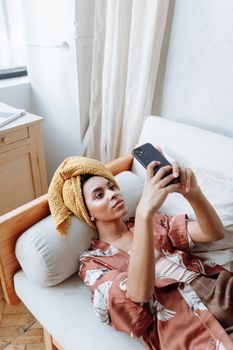 A woman in a robe with a head towel taking a selfie indoors.