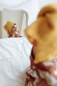 Woman in yellow towel looking into a mirror, capturing elegance and introspection.
