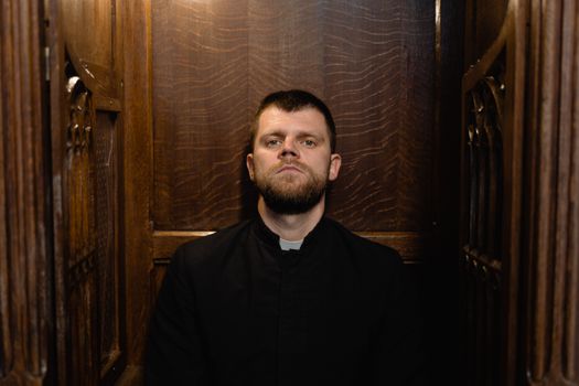 A priest sits solemnly in a classic wooden confessional, embodying faith and tradition.