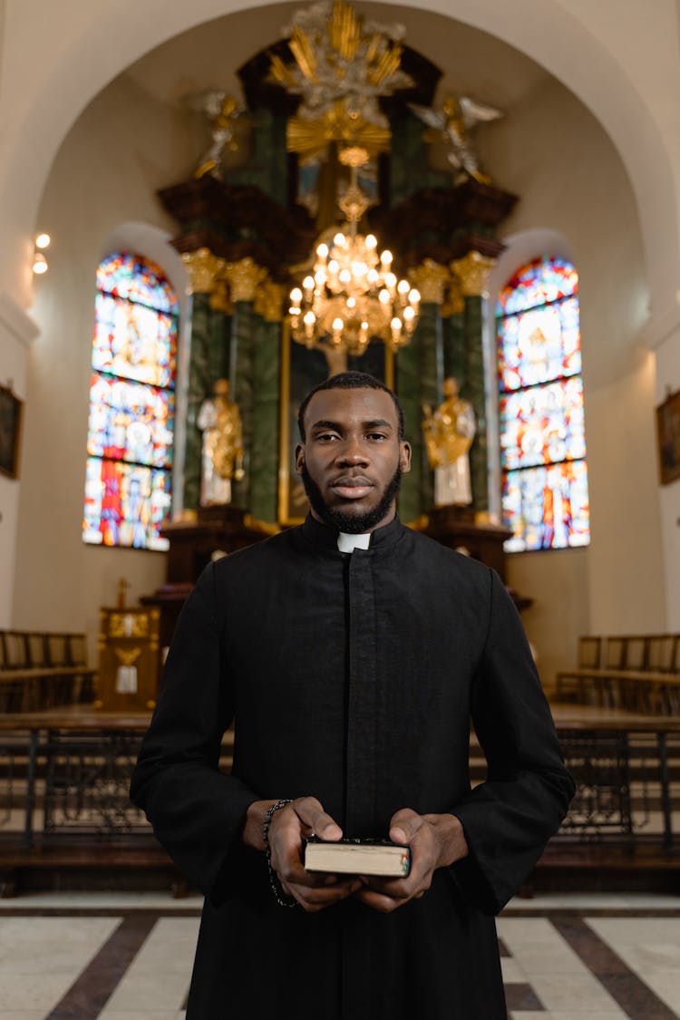 A Man In A Cassock Holding A Bible