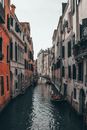 Bridge above rippled water channel with boats between aged stone building exteriors in Venice Italy