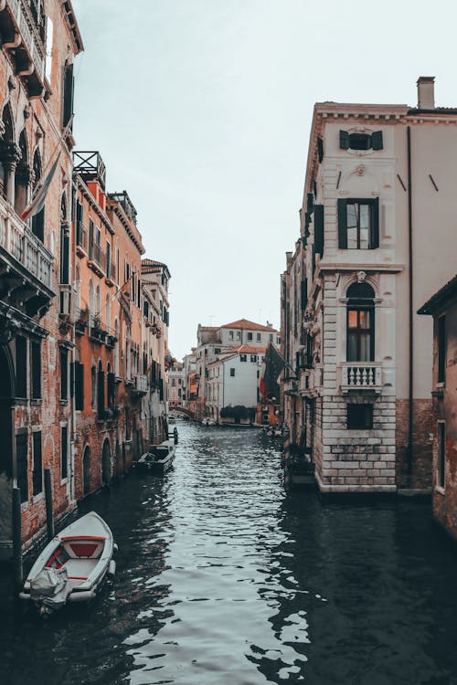 Free Boats on canal with ripples between old multistory stone building facades under light sky in Venice Stock Photo