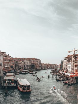 Ferries and motorboat sailing on rippled water channel between aged buildings under cloudy sky in urban port of Venice