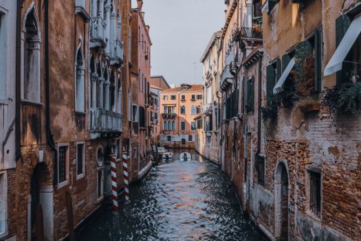 Rippled water channel between aged building exteriors with rough brick walls and columns in Venice Italy