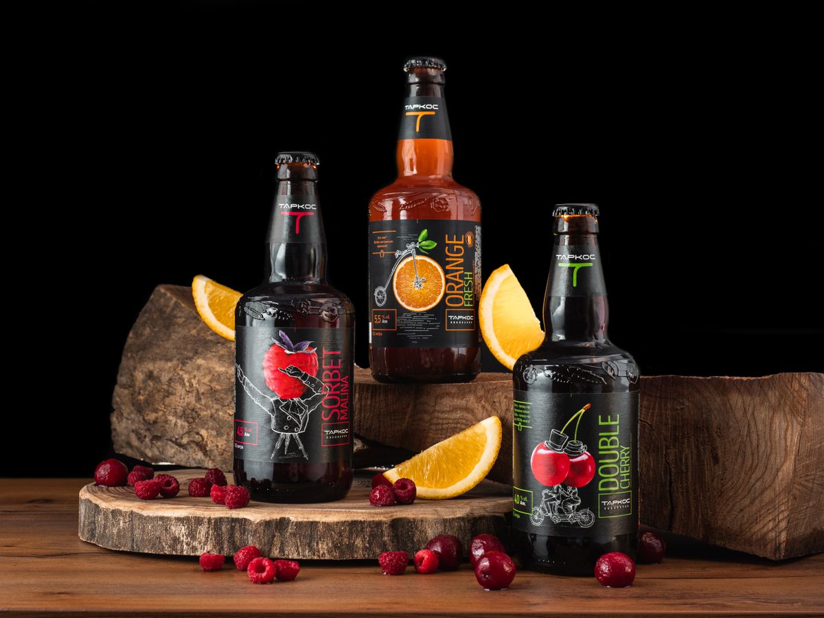Three craft fruit beer bottles styled with fresh citrus and berries on timber blocks