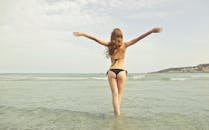 在马耳他姆加尔，一名穿着比基尼的女子站在大海中，举起双臂，享受着阳光明媚的一天