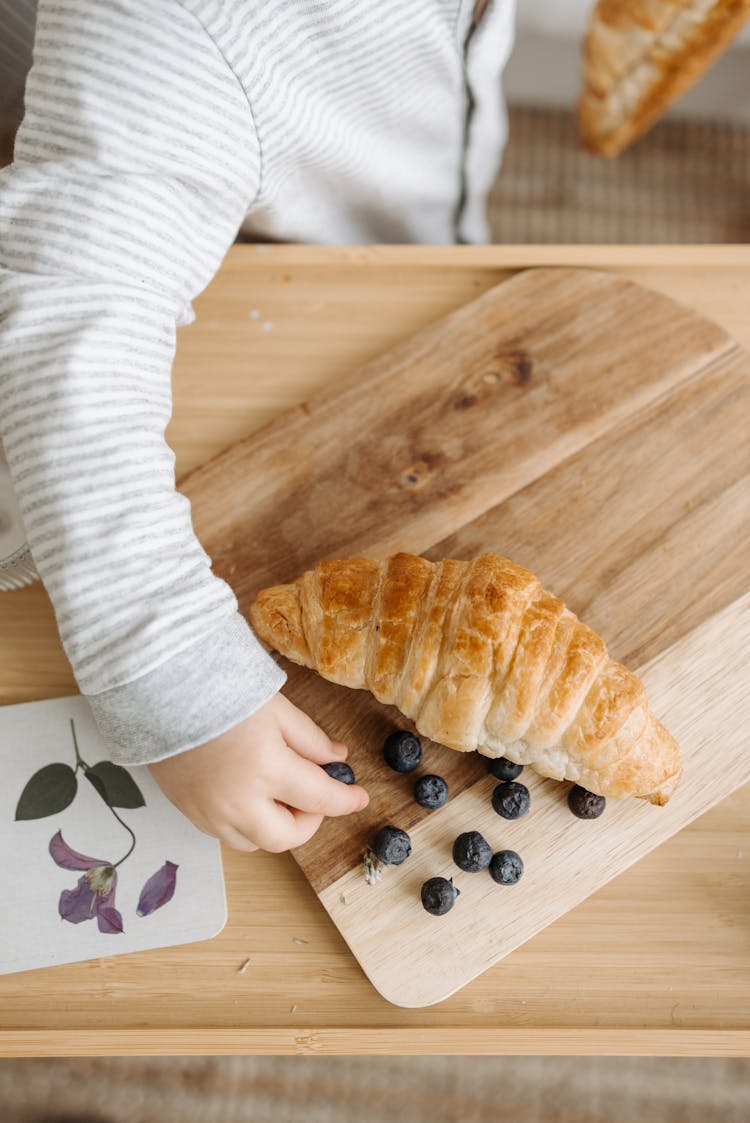 A Kid Getting Blueberries From A Wooden Chopping Board