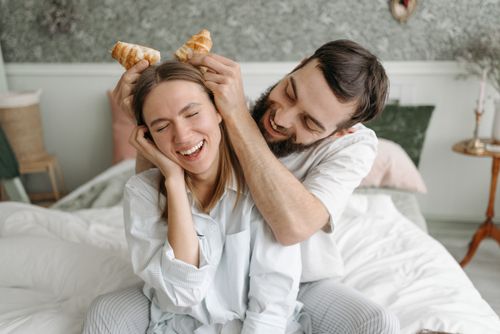Free Joyful couple having fun with croissants on a cozy morning in bed. Stock Photo