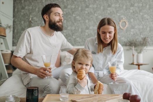 A family enjoying breakfast in their bedroom, featuring croissants and orange juice.