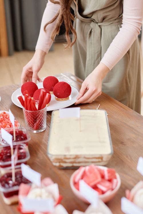 Free Elegant dessert table with red cakes and snacks being arranged by woman in a cozy setting. Stock Photo