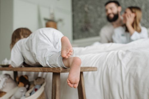 Free Adorable child climbing in a cozy bedroom with parents in the background. Stock Photo