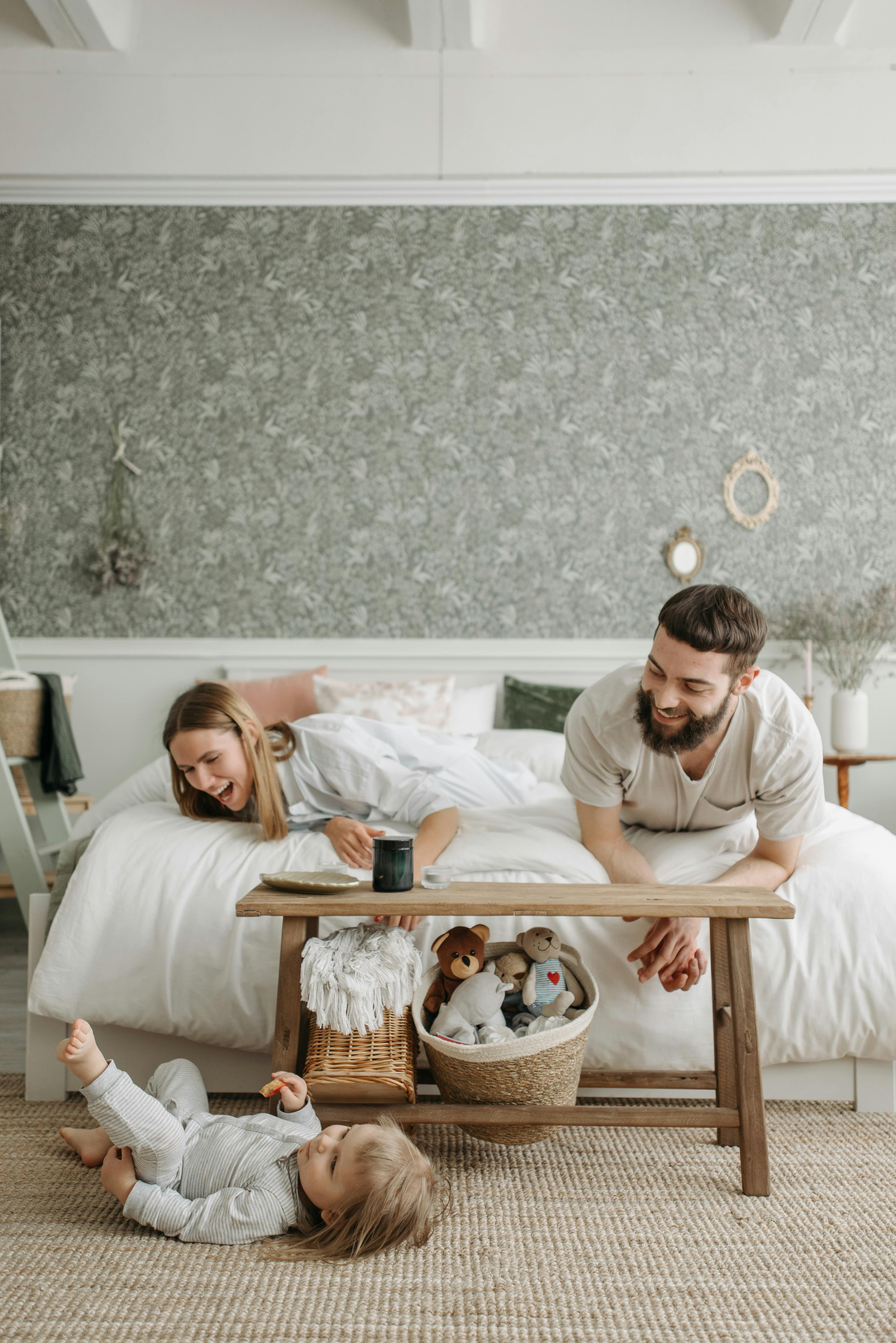 a couple lying on the bed while looking at their daughter lying on the floor