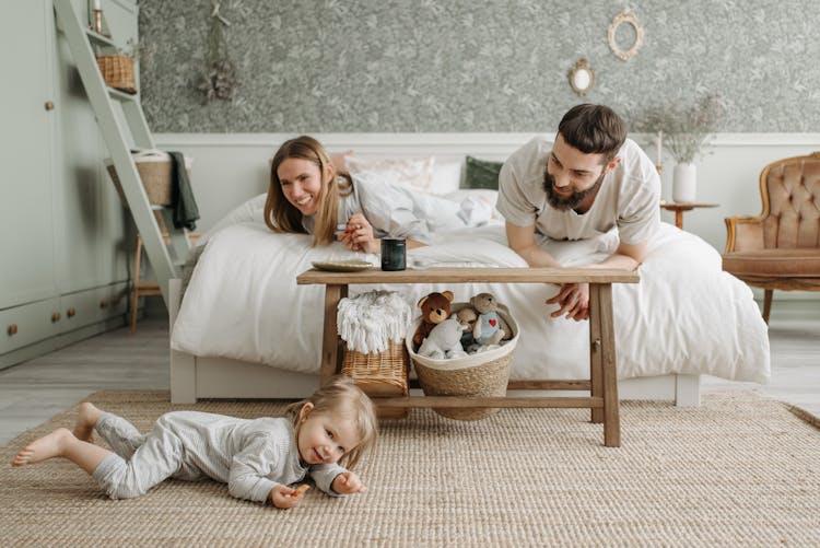 A Couple Lying On The Bed While Looking At Their Daughter Crawling On The Floor