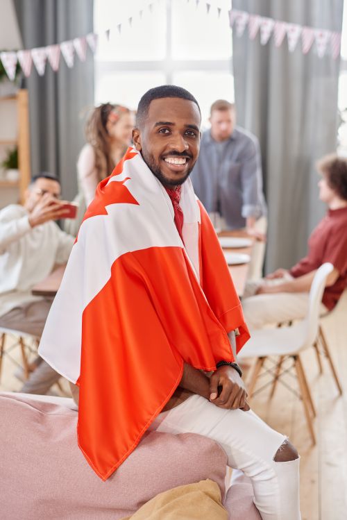 Free Cheerful man wearing Canadian flag cape at a social gathering indoors, exuding national pride. Stock Photo