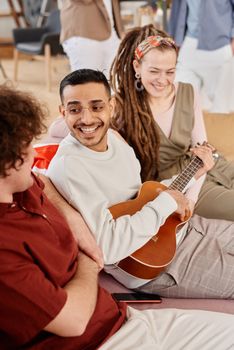 Diverse group of friends enjoying music and conversation indoors, smiling and relaxed.