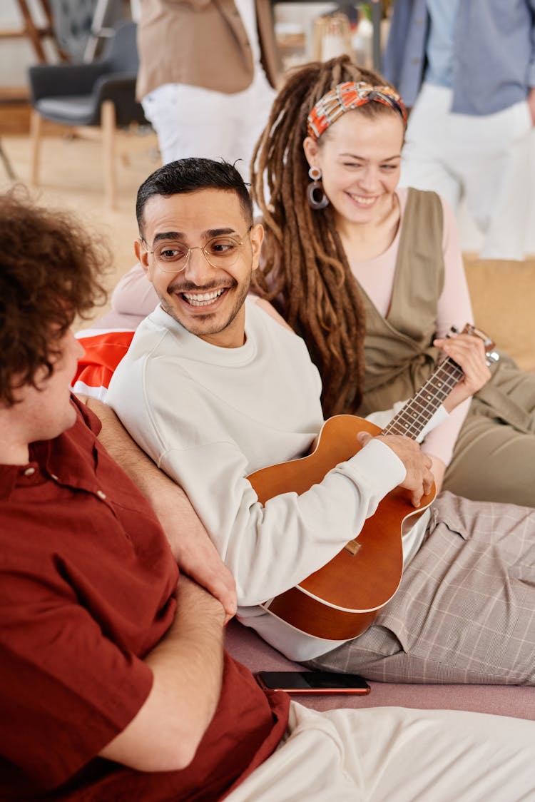 Man In White Sweater Playing A Guitar While With Friends