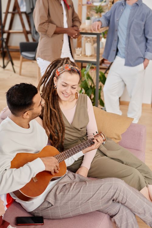 Free Group of friends relaxing indoors, one playing guitar and engaging with others. Stock Photo