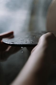 Detailed view of water droplets dripping from a glass surface held by hands.