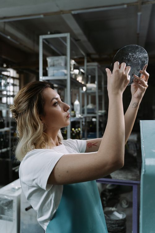 Free A woman carefully examines a metal disc in an industrial workshop setting. Stock Photo