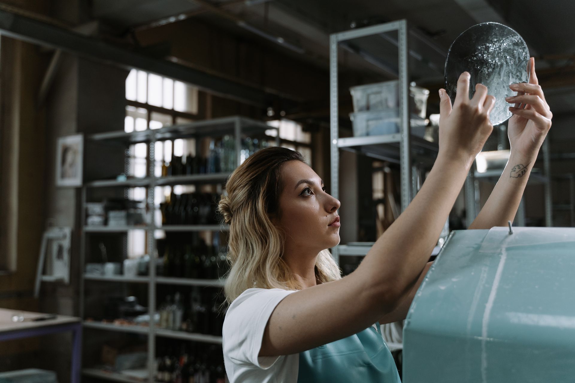 A woman examines a piece of glass in an industrial workshop setting.