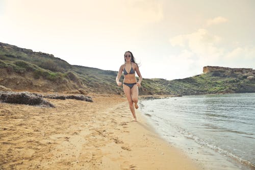 白い砂の海岸で走っている灰色のビキニを着ている女性