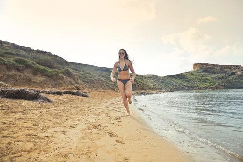 Free Woman in sunglasses and bikini running on a beautiful sandy beach in Mgarr, Malta. Stock Photo