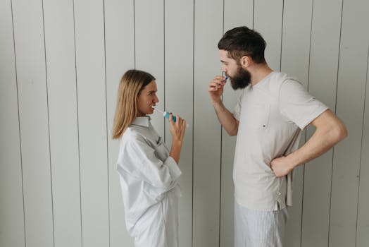 A couple brushing their teeth indoors, sharing a morning routine. Side view highlights interaction.