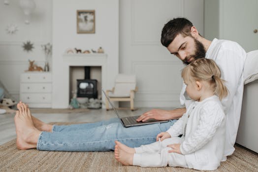 A father and daughter bonding while using a laptop in a cozy living room setting.