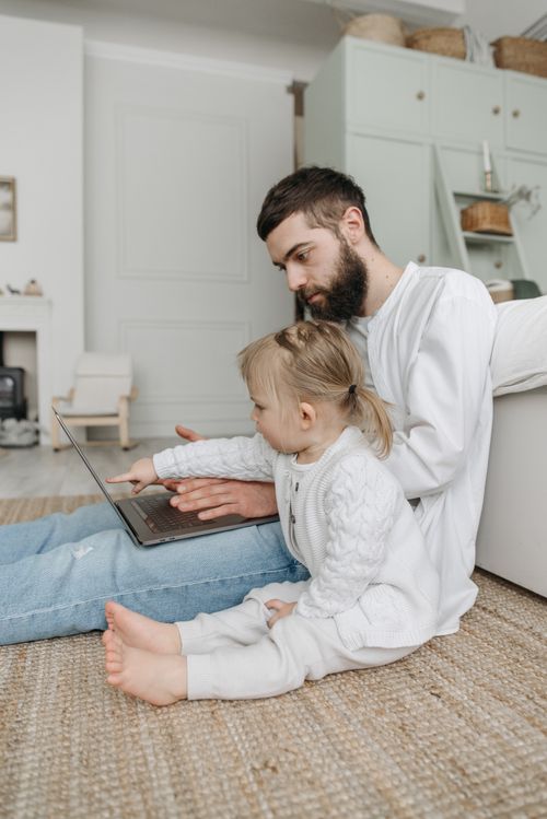 Free Father and daughter enjoying quality time on the floor with a laptop, fostering bonding and learning. Stock Photo