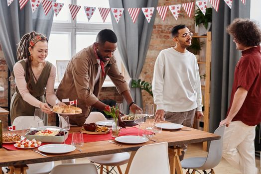 A diverse group of friends enjoying a festive Canada Day celebration indoors, sharing food and laughter.