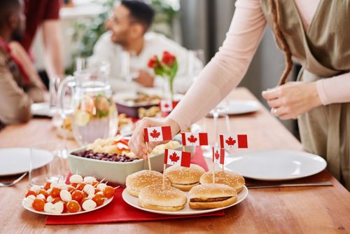 Free Festive Canadian dinner party scene with burgers, flags, and a lively gathering around the table. Stock Photo