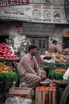 A smiling fruit vendor at a bustling street market in Lahore, Pakistan.