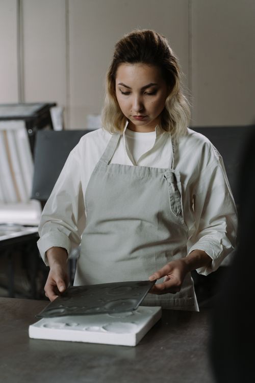 Free A young craftswoman in an apron molds materials in a workshop setting, showcasing artisanal skills. Stock Photo