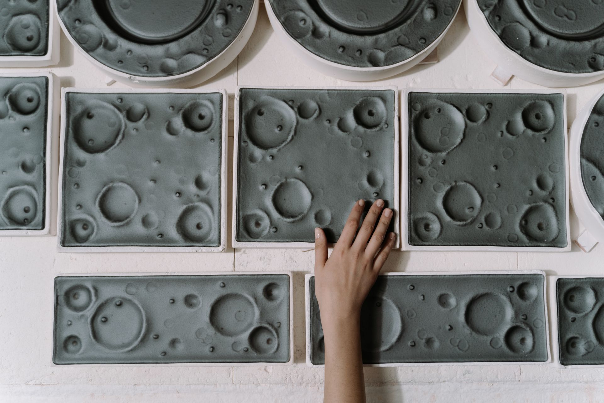 A hand touching handcrafted ceramic plates with unique lunar surface patterns, showcasing craftsmanship.